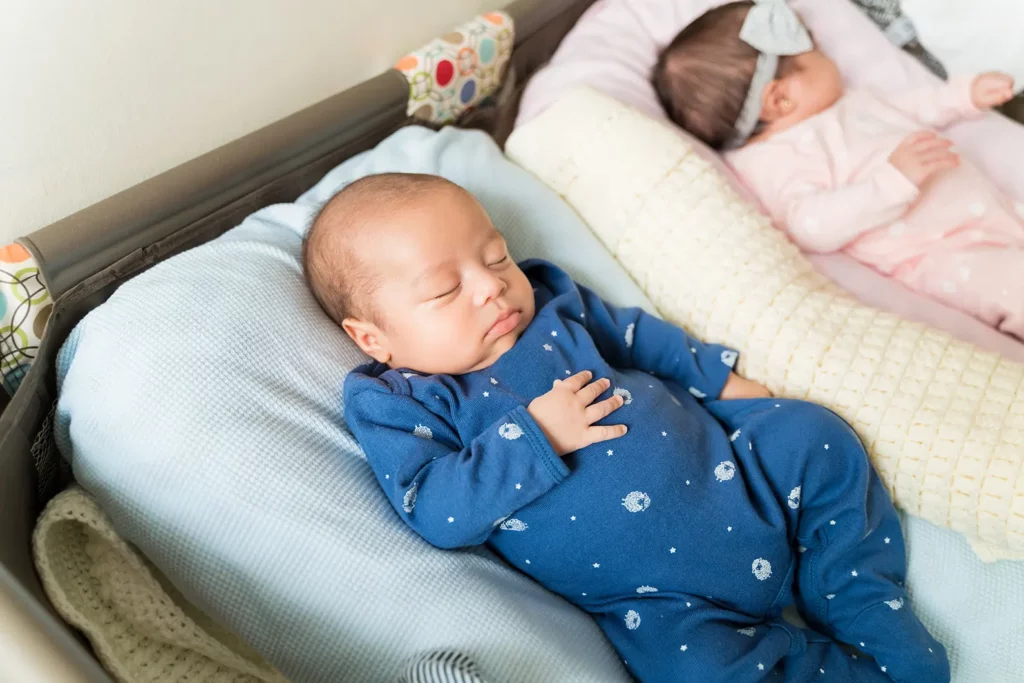 Deux bébés dorment paisiblement côte à côte dans un lit, sous la surveillance d’un adulte