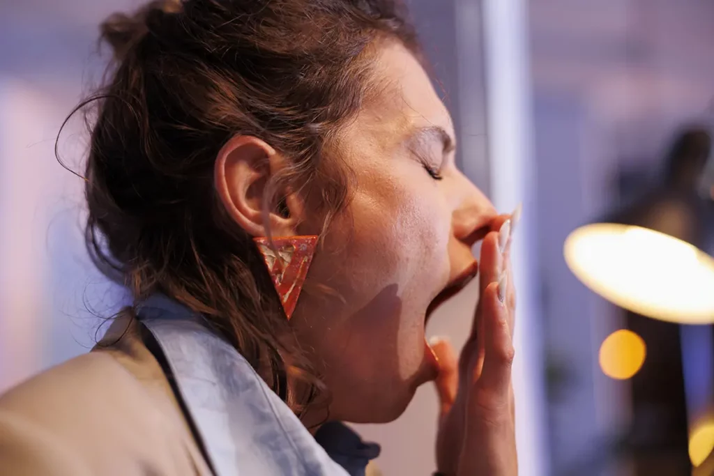 Une femme épuisée bâille en se couvrant la bouche avec la main, illustrant la fatigue intense, possiblement liée au manque de sommeil ou au stress