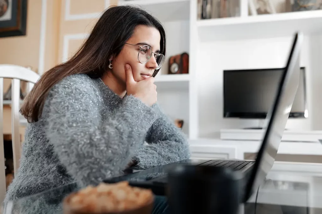 Jeune maman concentrée devant son ordinateur portable, effectuant des démarches administratives pour rattacher son bébé à la sécurité sociale depuis son salon
