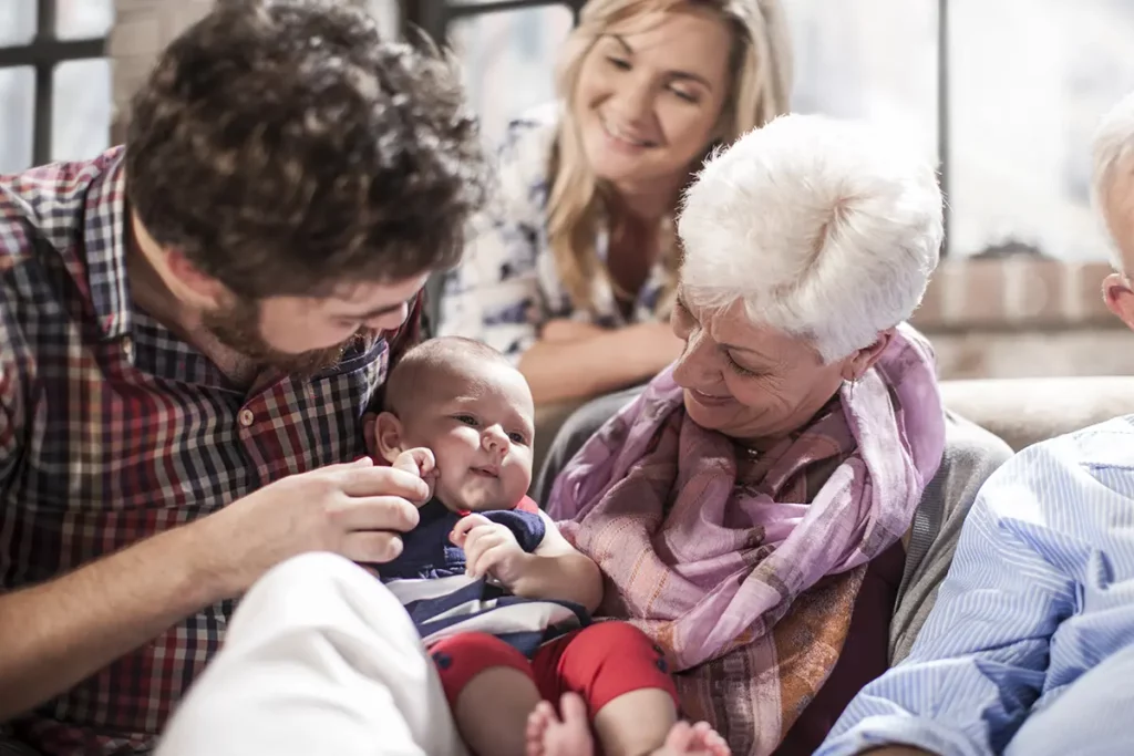 Bébé souriant dans les bras de sa grand-mère entouré de ses parents et grands-parents
