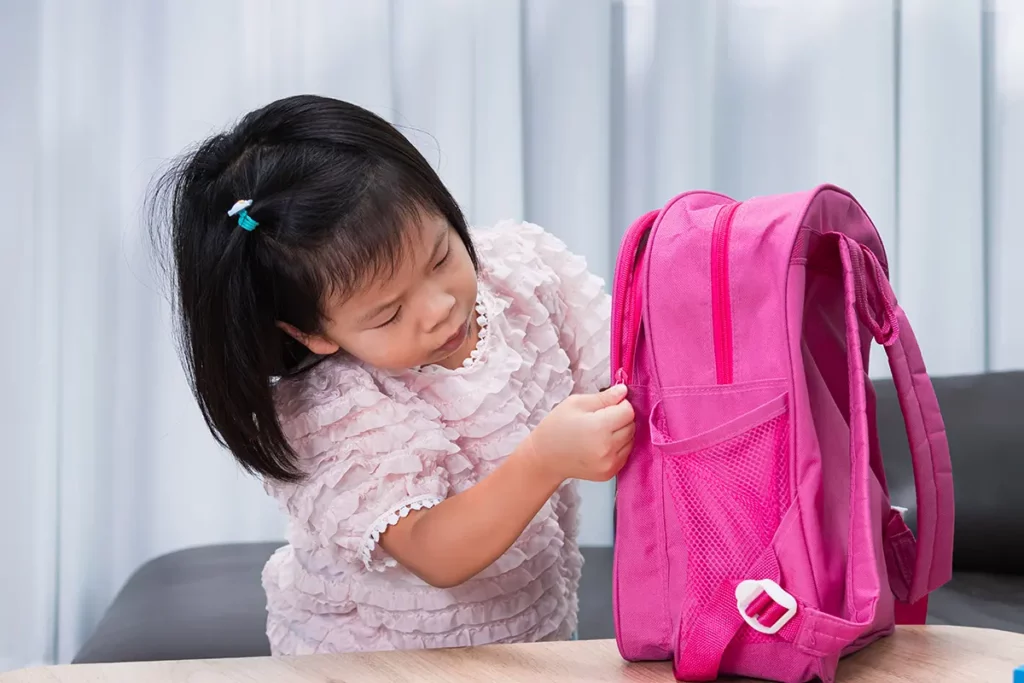 Jeune fille concentrée qui prépare son sac à dos rose pour la rentrée scolaire