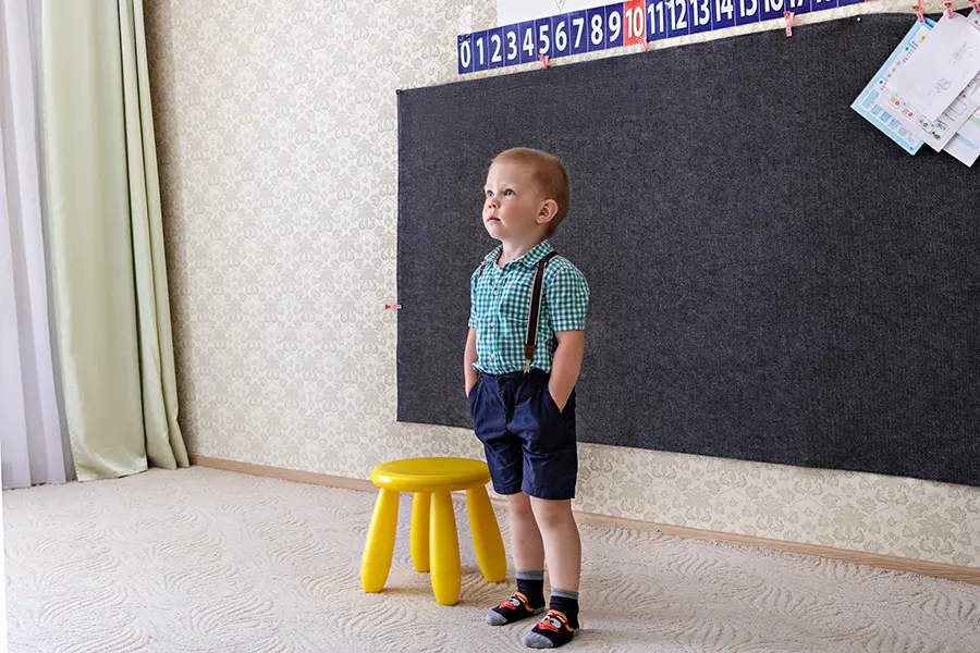 Jeune garçon en tenue soignée debout dans une classe de maternelle près d’un tableau pour se présenter