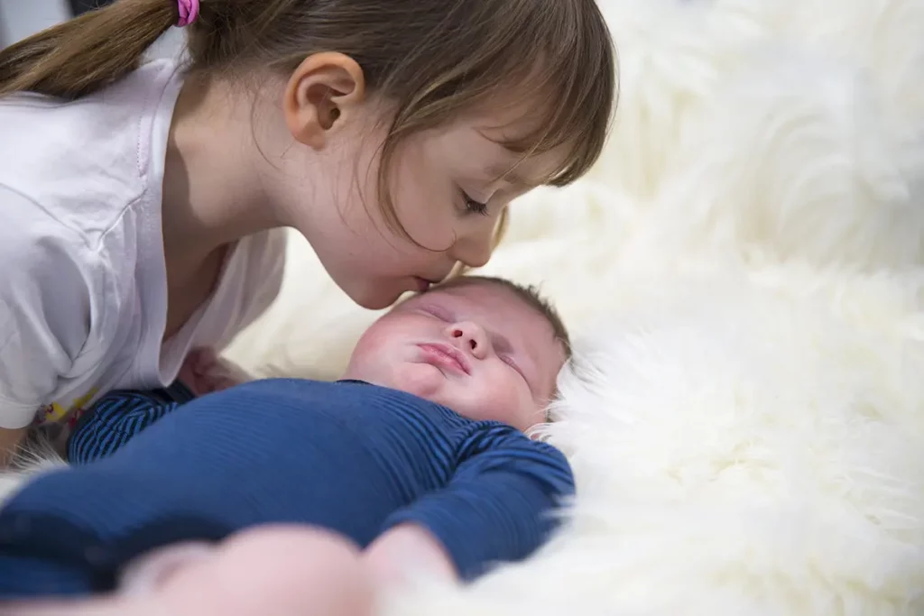 Petite fille embrassant tendrement son petit frère nouveau-né endormi sur une couverture blanche