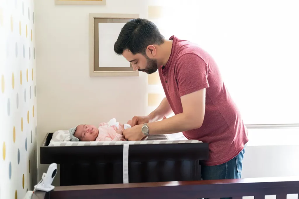 Papa change la couche de son bébé sur la table à langer dans la chambre