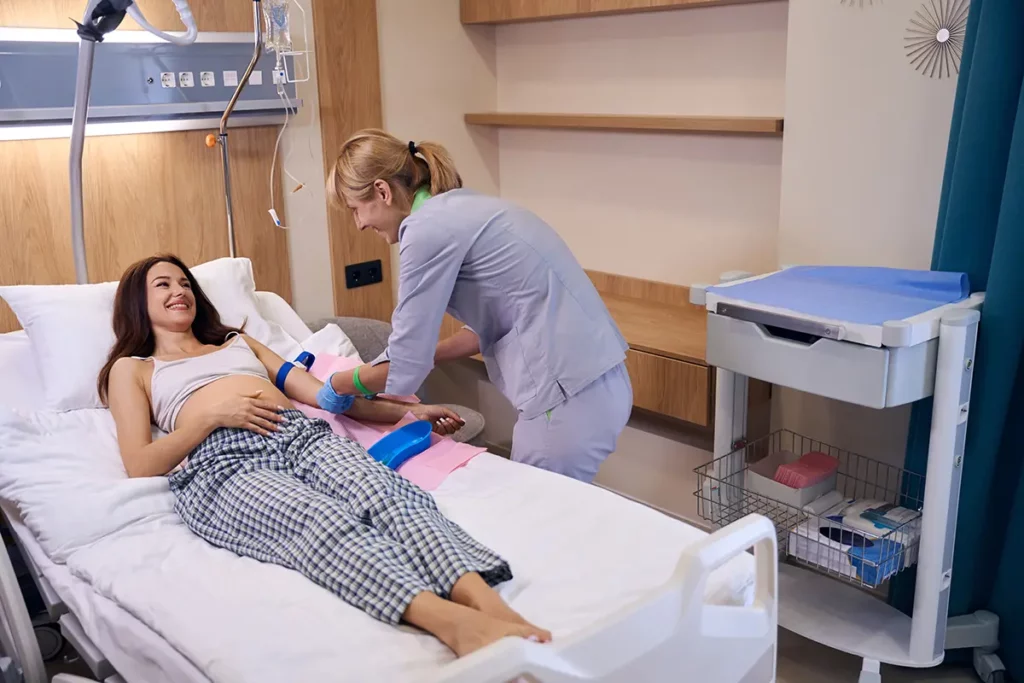Sage-femme souriante qui aide une femme enceinte allongée sur un lit d’hôpital en la préparant pour l’accouchement