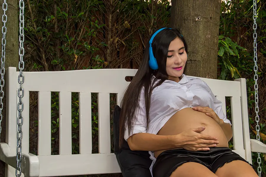 Femme enceinte qui se repose sur un banc, en train d'écouter de la musique douce avec un casque.
