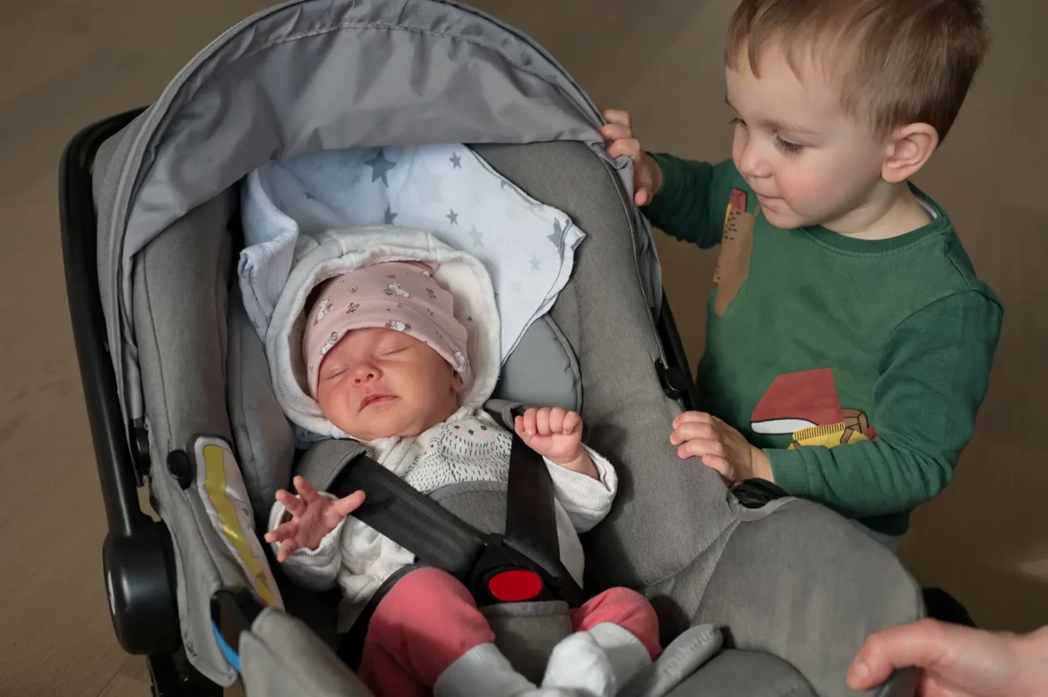 Un nouveau-né dort dans une poussette, accompagné de son grand frère qui la regarde.