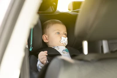 Un bébé assis dans un siège auto, regardant par la fenêtre avec une tétine dans la bouche, prêt pour un voyage en voiture