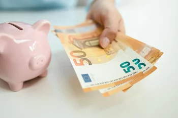 CAF qui verse de l’argent Main tenant des billets de 50 euros à côté d'une tirelire rose en forme de cochon, symbolisant le versement d'aides financières comme celles de la CAF