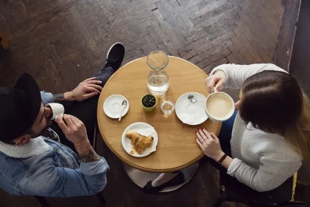 Couple discutant des démarches complémentaires avant la naissance Vue de dessus d’un couple assis à une table de café, buvant un café et échangeant à propos des dernières démarches administratives à préparer avant l’arrivée de leur bébé