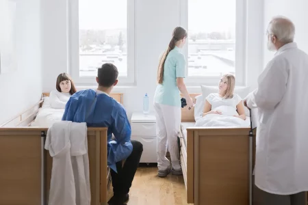 Deux femmes enceintes dans la même chambre d'hôpital, discutant avec du personnel soignant