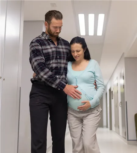 Femme enceinte soutenue par son compagnon dans un couloir d’hôpital en route pour la maternité