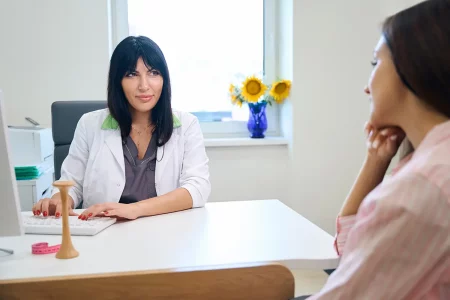 Femme en consultation chez la gynécologue Une femme assise en face d'une gynécologue en blouse blanche lors d'une consultation médicale, dans un cabinet lumineux et accueillant