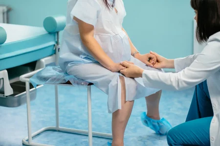 Femme enceinte en blouse médicale essayant une position assise avec l’aide d’une soignante pour faciliter le travail avant l’accouchement