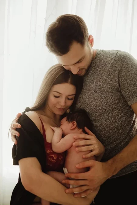 Jeune couple enlacé tenant tendrement leur nouveau-né contre eux, la mère allaite le bébé pendant que le père les entoure de ses bras