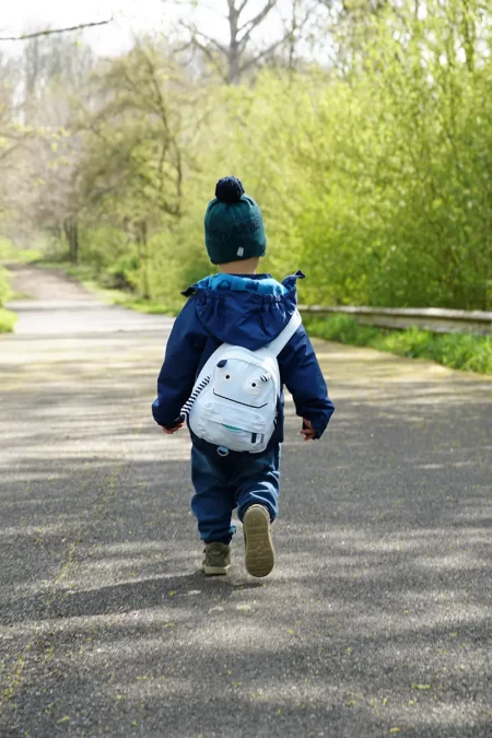 Petit garçon portant un sac à dos blanc marchant seul sur un chemin en forêt