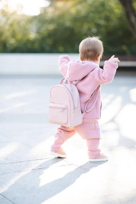 Petite fille en jogging rose avec sac à dos qui marche seule sur le chemin de l’école
