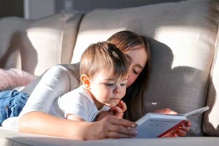 Grande sœur lisant une histoire à son petit frère allongés sur le canapé